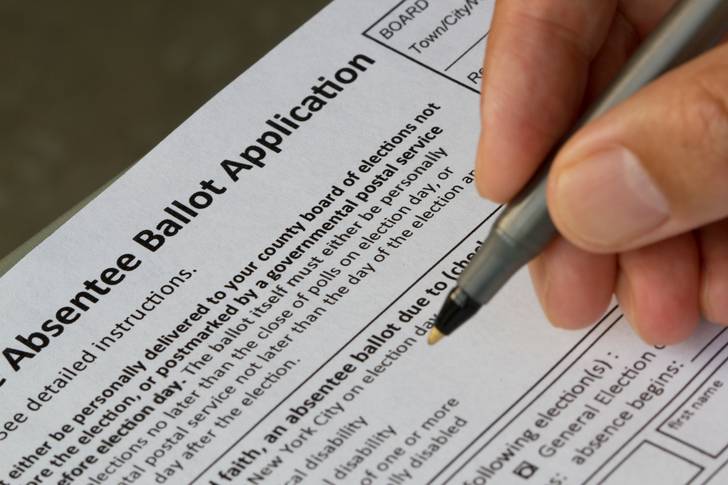 A hand holding a pen as it fills out an absentee ballot application